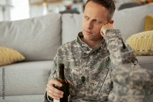 Depressed soldier with bottle sitting in livig room., Alcohol addiction.. photo