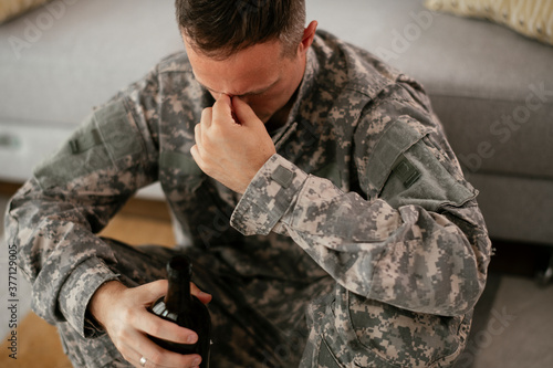 Depressed soldier with bottle sitting in livig room., Alcohol addiction..