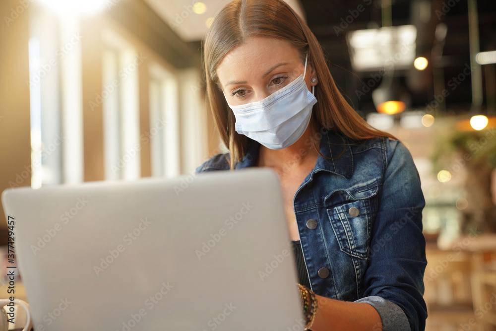 Young woman sitting at coffee shop and working on laptop with face mask Young woman sitting at coffee shop and working on laptop with face mask