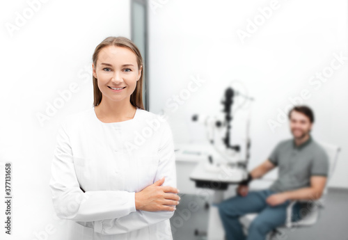 Portrait of a beautiful woman ophthalmologist in a modern ophthalmological office  in the background a handsome male patient is sitting