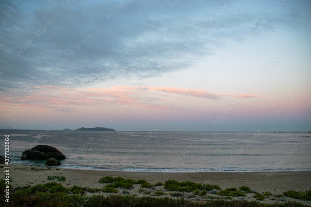 Photo of the beach in Galicia during sunrise. Beautiful pink and yellow clouds, empty beach. Amazing light during holidays.