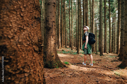 Full-length portrait of a young man in casual clothes and hiking walks through the woods to the mountains, stopped to rest and looks away.Hipster guy walking in the untouched forest, active recreation