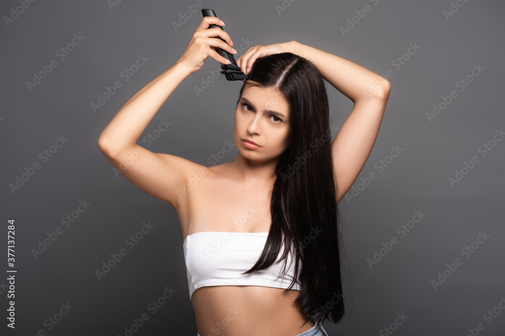 Fototapeta premium sad brunette long haired woman shaving head with electric razor isolated on black