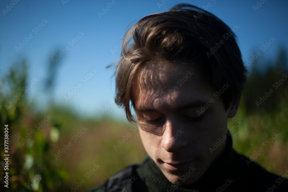 Portrait of a guy in the sunlight. Young man in nature. A student is skipping school in the woods. A guy with a regular haircut. A young man of European appearance. A man on a summer day.