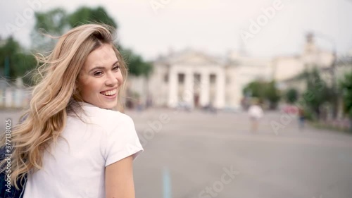 Young pretty cheerful girl smiles, turns around. Follow me, point of view shot. Happy blonde female student on campus walking down the street. 
