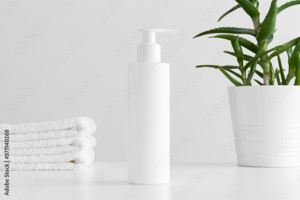 White cosmetic shampoo dispenser bottle mockup with a aloe vera and towels on a white table. White cosmetic shampoo dispenser bottle mockup with a aloe vera and towels on a white table.