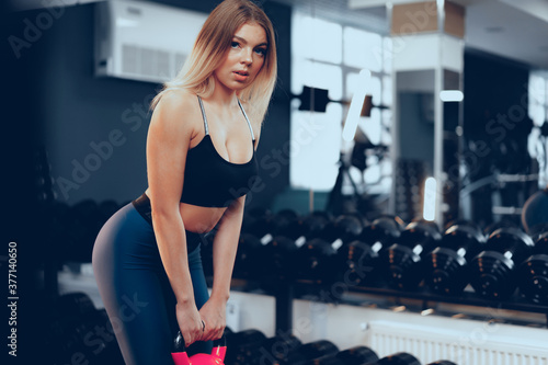Curvy fit young blonde woman lifting dumbbell in a gym