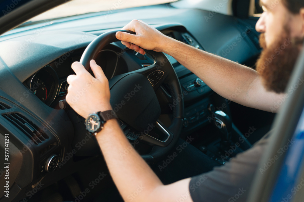 Close up photo of young bearded man with hands on steering wheel