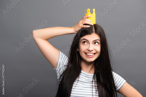 brunette long haired woman in paper crown smiling isolated on black