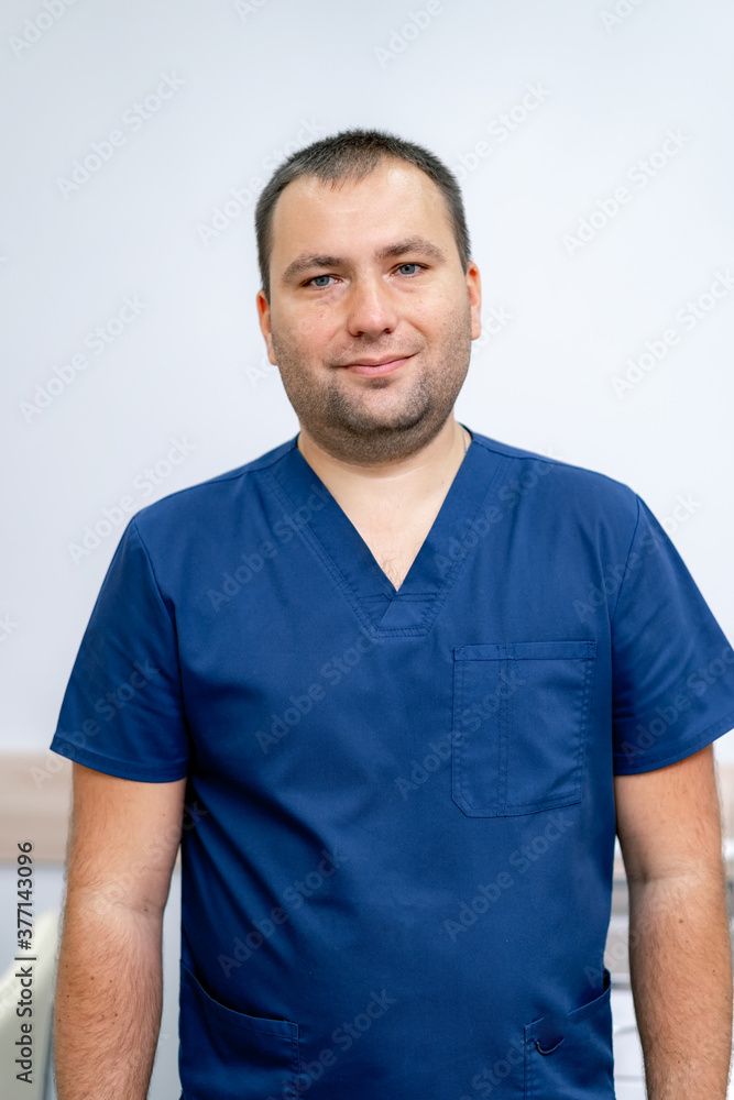 Fototapeta premium Portrait of a male doctor in hospital. Man looking at camera and smiling. White wall background. Closeup.
