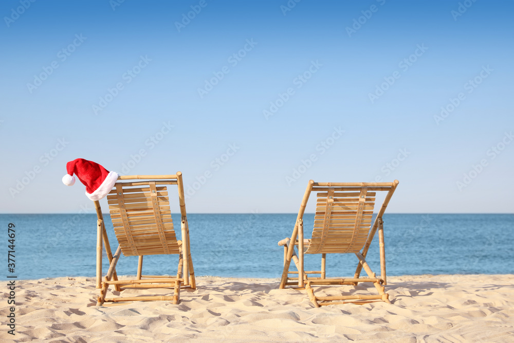 Sun loungers and Santa's hat on beach, space for text. Christmas vacation