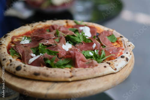 close up pizza with cured meats, arugula and cheese. On wooden plate. Defocused background