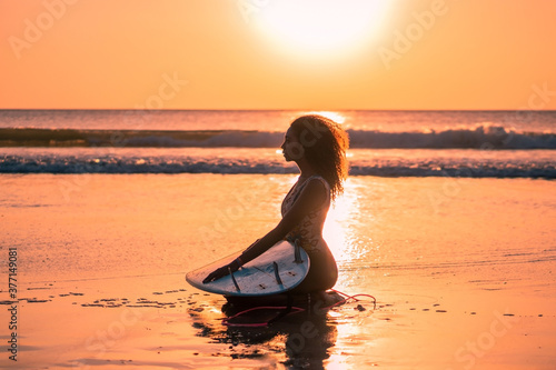 Portrait of woman surfer with beautiful body on the beach with surfboard at colorful sunset. © Lila Koan
