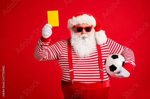Portrait of his he nice handsome bearded fat overweight Santa grandfather playing football showing yellow card whistling isolated over bright vivid shine vibrant red color background © deagreez