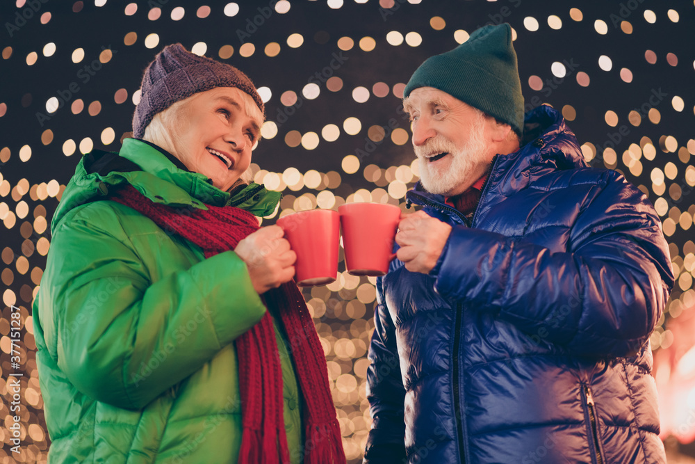 Two old people grey white hair parents retired pensioner man woman date x-mas christmas evening jolly walk under garland lights outdoors toast eggnog beverage mug