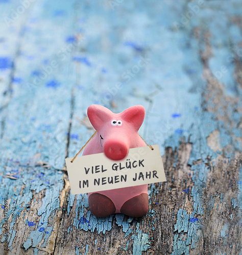 Kleines rosa Glücksschwein, mit Tafel und Aufschrift: Viel Glück im neuen Jahr, auf altem, blauen Holz.