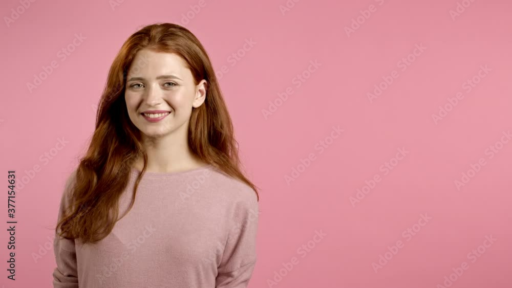 Copy space. Young smiling woman with red hairstyle looking to camera. Portrait of cute beautiful girl on pink studio wall background. Copy space. Young smiling woman with red hairstyle looking to camera. Portrait of cute beautiful girl on pink studio wall background.
