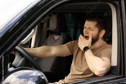 Tired man yawning while driving his modern car