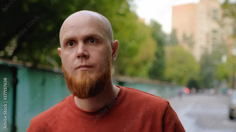 A young bald guy with a red beard in a dark orange sweater looks thoughtfully in anticipation of someone. Calm emotion. Walk on a summer evening. A young bald guy with a red beard in a dark orange sweater looks thoughtfully in anticipation of someone. Calm emotion. Walk on a summer evening.