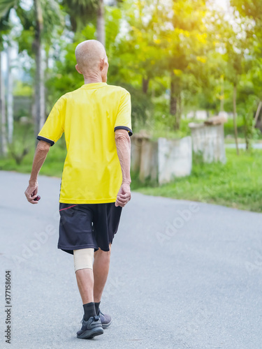 Back view portrait of a Asian elderly man in fitness wear walking and jogging for good health in public park. Senior jogger in nature. Older Man enjoying Peaceful nature. Healthcare concept.