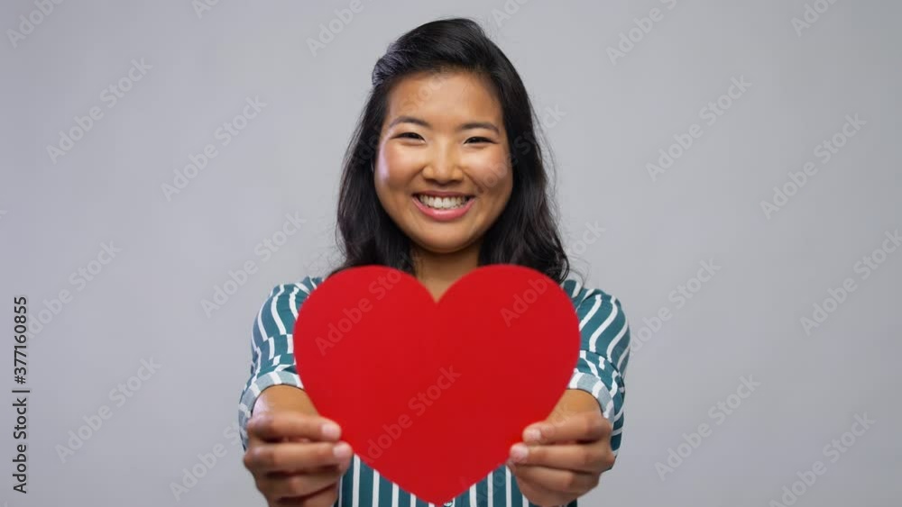 love, charity and valentines day concept - happy asian young woman with red heart over grey background love, charity and valentines day concept - happy asian young woman with red heart over grey background