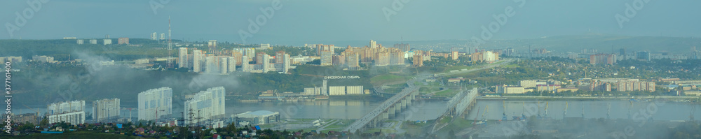 Panorama of city of Krasnoyarsk in Russia at sunrise. Yenisei River, fog. Nikolaevsky bridge connect  Oktyabrsky and Sverdlovsky districts of Krasnoyarsk. Text in Russian 