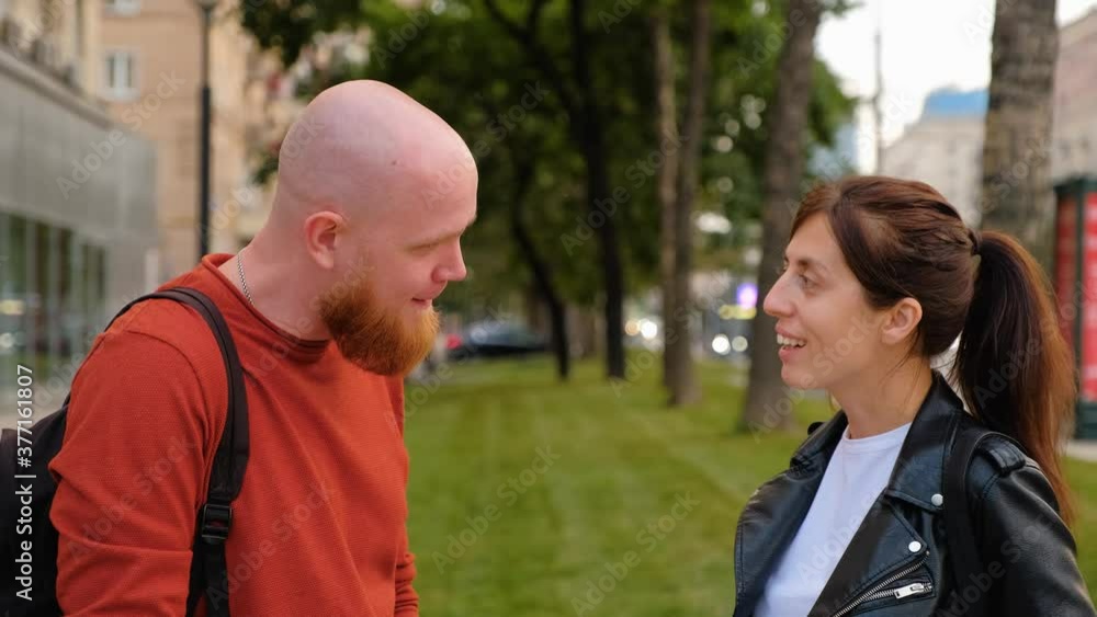 Dialogue on the street between a young brutal bald guy with a red beard and a brunette girl in a black leather jacket. Ask and answer. Positive emotions. Summer clear day. Dialogue on the street between a young brutal bald guy with a red beard and a brunette girl in a black leather jacket. Ask and answer. Positive emotions. Summer clear day.