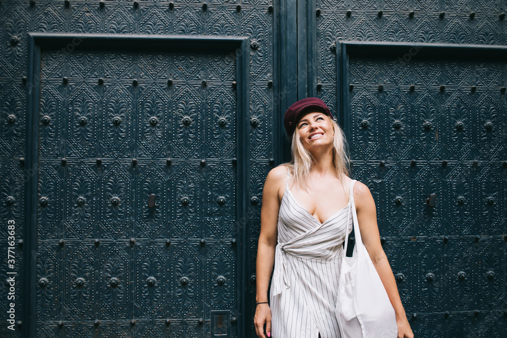 Cheerful female traveller with stylish eco bag laughing near architecture with ancient doors in historic center, trendy dressed hipster girl visiting touristic town satisfied with getaway trip Cheerful female traveller with stylish eco bag laughing near architecture with ancient doors in historic center, trendy dressed hipster girl visiting touristic town satisfied with getaway trip