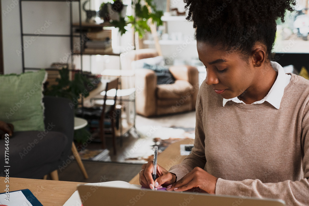 Female student studying for online exam using stationary and notepad siting in front on laptop in modern kitchen. Female student studying for online exam using stationary and notepad siting in front on laptop in modern kitchen.