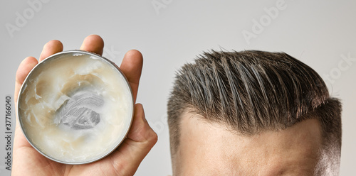 Man applying a clay, pomade, wax, gel or mousse from round metal box for styling his hair after barbershop hair cut. Advertising concept of mans products. Treatment and care against lost of hair