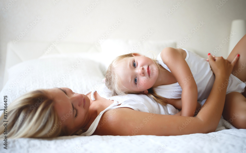 young woman hugs with her daughter on a white bed young woman hugs with her daughter on a white bed