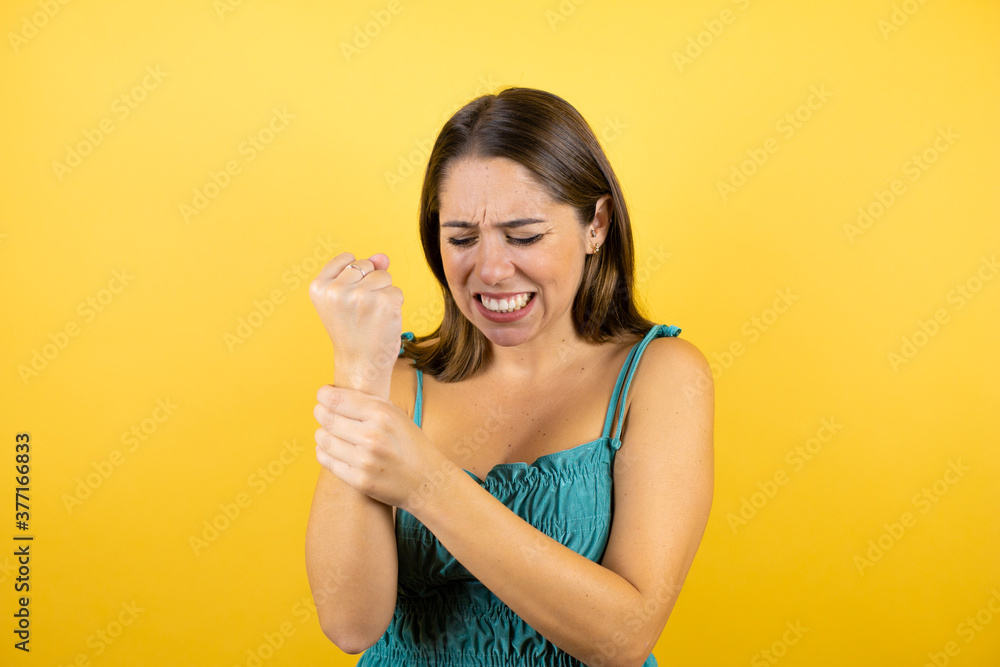 Young beautiful woman over isolated yellow background suffering pain on hands and fingers, arthritis inflammation Young beautiful woman over isolated yellow background suffering pain on hands and fingers, arthritis inflammation