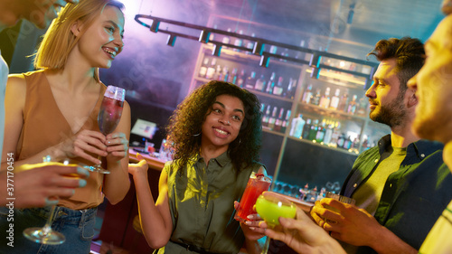 A group of friends, young women and men chatting while having fun, drinking cocktails, spending time in the night club
