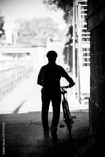 Silhouette of man walking with bicycle in hand in the street