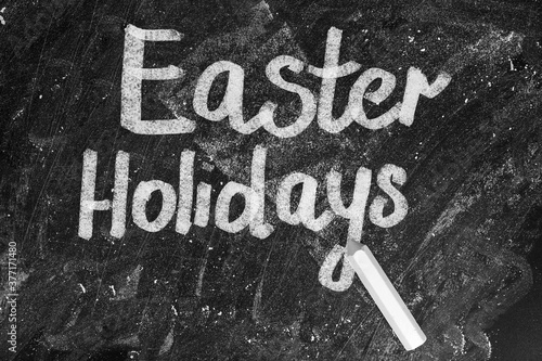 Text Easter Holidays and chalk on blackboard, top view. School break