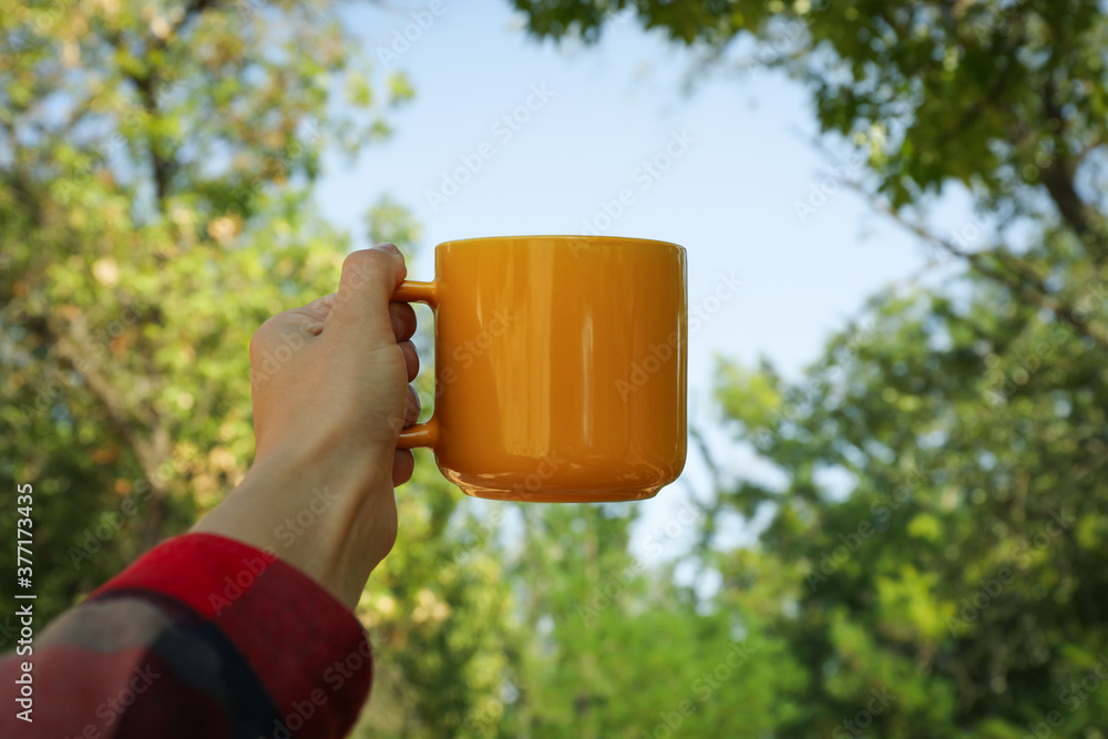 Obraz premium Female hand in shirt hold yellow cup outdoor