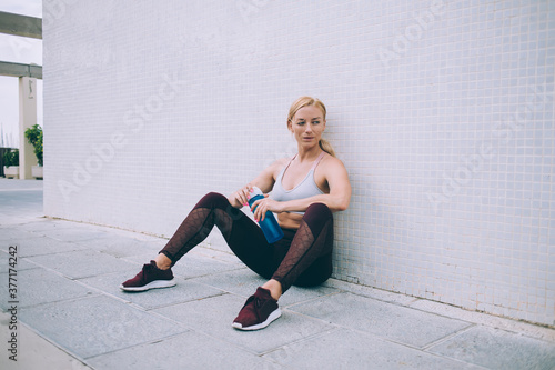 Good looking bodybuilder with perfect slim figure resting at city urbanity, Caucasian female athlete with muscular body holding water tumbler thinking about crossfit exercises for energy workout