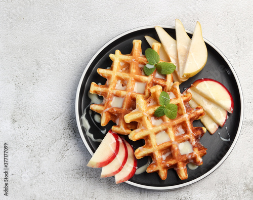 Viennese waffles served with fruits on a round plate on a light gray background. Top view, flat lay
