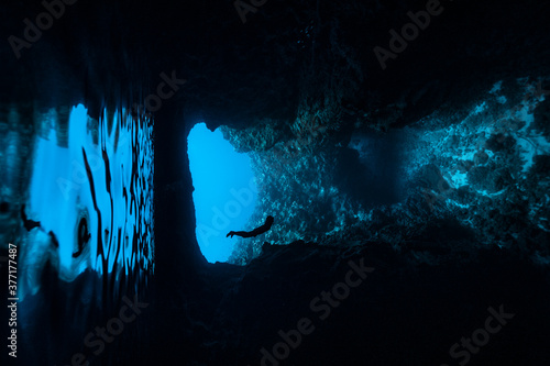 A female freediver diving into the cave with backlit