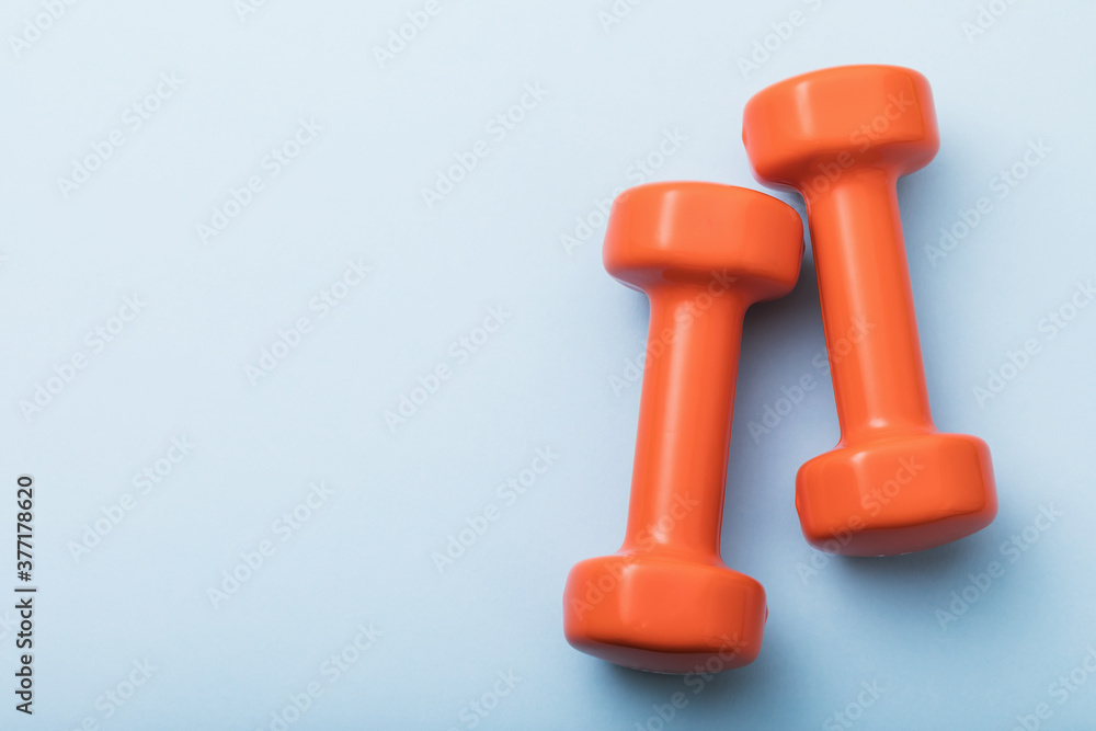 Orange dumbbells on a blue background with copy space, top view Orange dumbbells on a blue background with copy space, top view