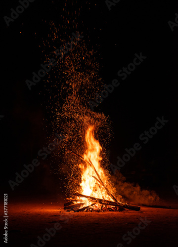 Camp fire in the night. Burning wood at night. Campfire at touristic camp at nature in dark. Flame amd fire sparks on black background. Hellish fire element. Fuel, power and energy