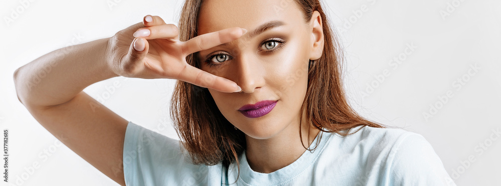 Fototapeta premium Hey smile you. Portrait of cute glamor girl brunette woman with fashion make-up purple lips winking happily showing peace victory gesture as fooling around, being optimistic. Beautiful female face.