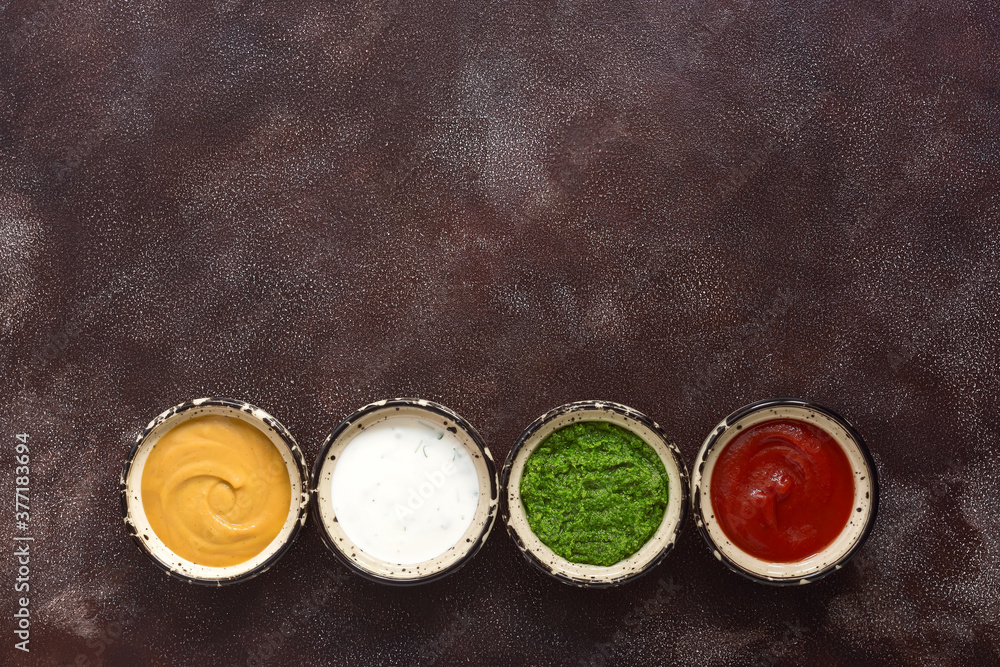 Collection of various sauces in the bowl: tomato, pesto, creamy with greens and mustard on a dark rustic background. Set of sauces in a line. Top view, copy space. Collection of various sauces in the bowl: tomato, pesto, creamy with greens and mustard on a dark rustic background. Set of sauces in a line. Top view, copy space.