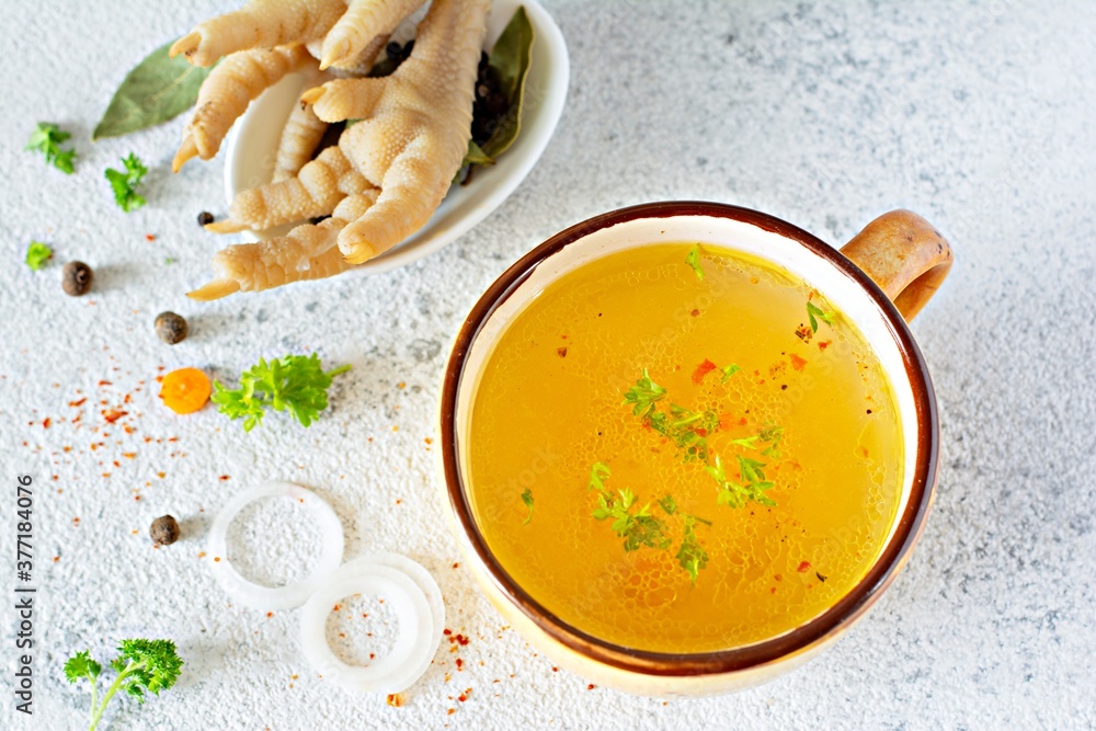 Homemade chicken (bone) broth/bouillon with vegetables, spices and herbs in a bowl (cup) on a light background. Natural collagen of animal origin. Liquid broth from meat, fish, vegetables. Homemade chicken (bone) broth/bouillon with vegetables, spices and herbs in a bowl (cup) on a light background. Natural collagen of animal origin. Liquid broth from meat, fish, vegetables.