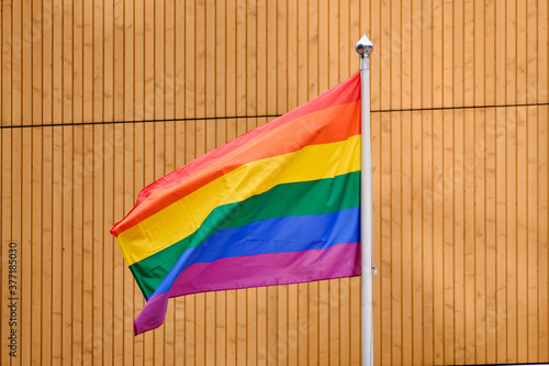 Obraz na płótnie The pride flag on a white flagpole against the wooden wall. w salonie