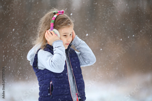 a little girl in warm headphones walks in the winter in a snowy Park and holds her head with her hands. hardening of children. photo