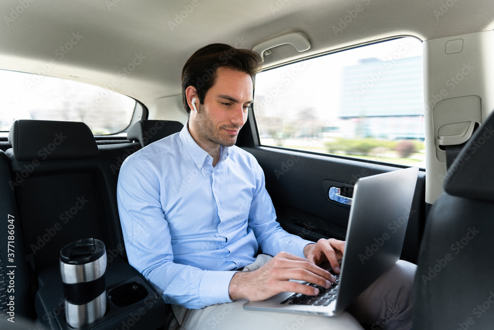 Young businessman sitting in taxi and using laptop Young businessman sitting in taxi and using laptop
