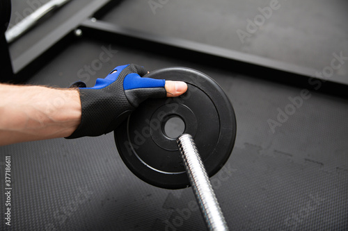 Male hand loading weight plate on a barbell. Heavy weight exercise on a black gym safe flooring mat.