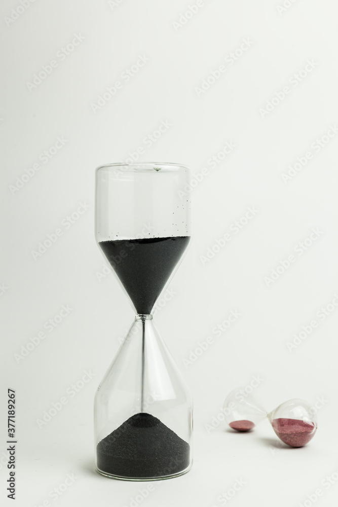 Vertical shot of two sand clocks made with glass on a white background. Time running and tempus fugit concept with copy space. Vertical shot of two sand clocks made with glass on a white background. Time running and tempus fugit concept with copy space.