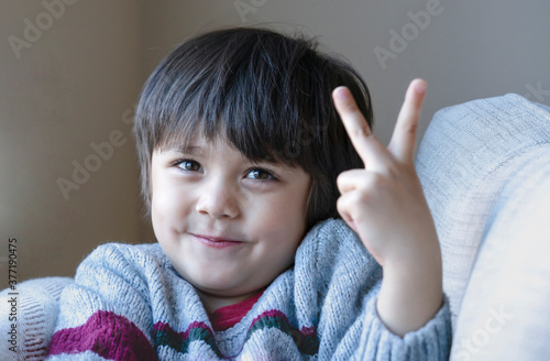 Portrait cute little boy looking at camear with smiling face, Selective focus Happy kid showing two fingers, Healhty child siting on osfa relaxing at home photo